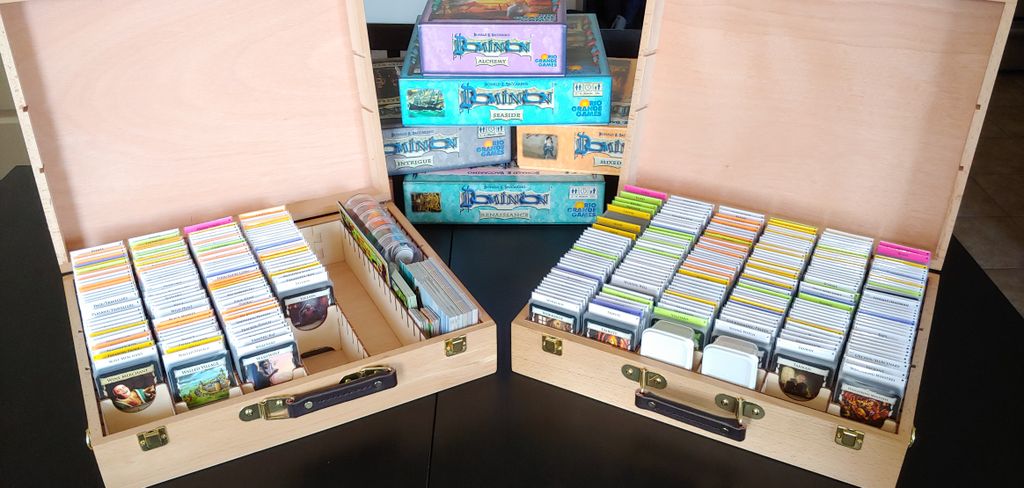 A picture of two wooden cases splayed open with all Dominion cards released before 2020 sleeved and organized within