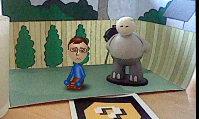 A picture of a Nintendo Mii version of Tylor Lilley kneeling in defeat in a diorama with a Strong Sad figure, taken with a Nintendo 3DS and AR card