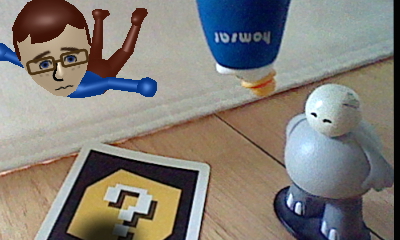 A picture of a Nintendo Mii version of Tylor Lilley floating with an upside down Homsar figure next to a Strong Sad figure, taken with a Nintendo 3DS and AR card