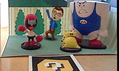 A picture of a Nintendo Mii version of Tylor Lilley celebrating in a diorama with a Strong Bad, Strong Mad, and The Cheat figure, taken with a Nintendo 3DS and AR card