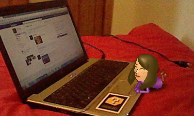 A picture of a miniature Nintendo Mii version of Leah Cramer browsing on a laptop with Facebook open on it, taken with a Nintendo 3DS and AR card