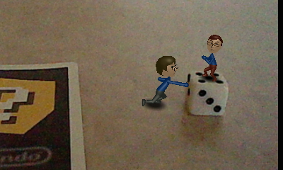 A picture of a miniature Nintendo Mii version of Tylor Lilley and Ethan Miller struggling to move a six sided die, taken with a Nintendo 3DS and AR card