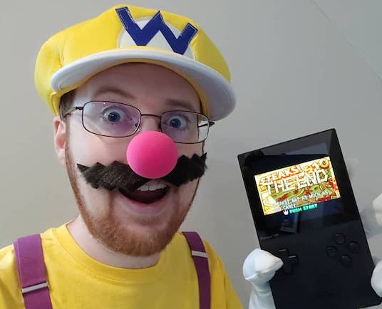 A picture of me dressed up as Wario, holding an Anlogue Pocket displaying Wario Land 4: Parallel World's THE END screen